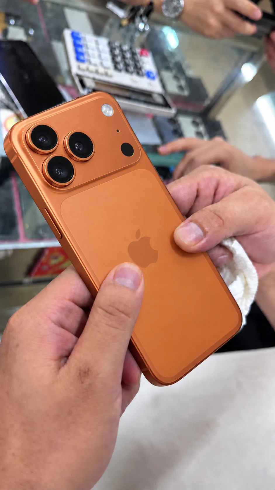 Illustrative image of a Cosmic Orange iPhone 17 Pro Max held over a phone counter